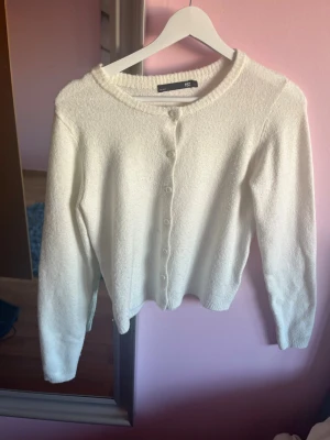 Vit kofta från lager 157 - Söt vit kofta från lager 157 med rund halsringning och knappar framtill. Koftan har lång ärm och är gjord i ett mjukt, stickat material som känns skönt mot huden. Perfekt att slänga över en topp för en enkel och clean look.