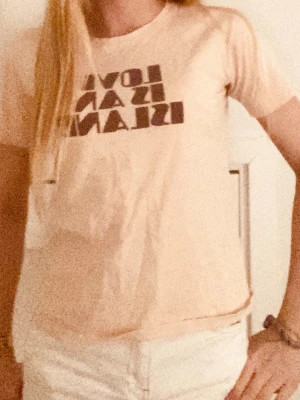 Beige t-shirt med tryck - Snygg beige t-shirt med svart texttryck framtill. Perfekt till jeans eller shorts för en avslappnad look. Köpt ifrån Bali.