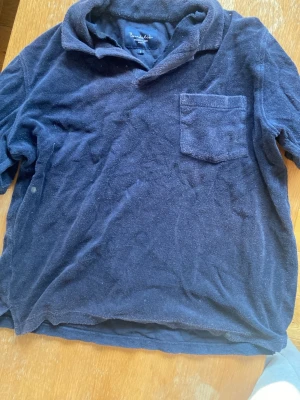 Mörkblå frottétröja från Bondelid - Mysig mörkblå tröja från Bondelid i frottéliknande material. Tröjan har krage, kort ärm och en bröstficka för en avslappnad look. Perfekt för dig som gillar klassisk och enkel stil.