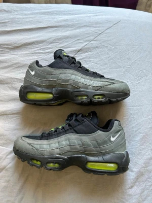 Nike Air Max 95 svart/grå sneakers - Nike Air Max 95 sneakers i svart och grått med neongula detaljer. Klassisk vågig design, synlig Air-dämpning i sulan och små vita Swoosh-loggor på sidan. Ovandelen är i en mix av textil och syntetmaterial. Skorna har svarta snören och coola detaljer på plösen. Köpte för 2100 från JD
