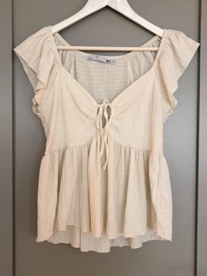 Beige blus med volang och knyt - Superfin beige blus från Lager 157. Jättefin men har ett fläckigt parti på ryggen då den är väl använd. Det borde gå bort med en tvätt med blekningsmedel🥰