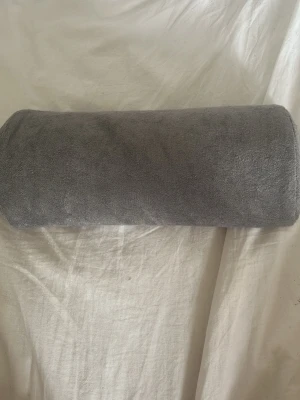 Grå cylinderformad kudde - Säljer en cylinderformad kudde i mjukt grått tyg med dragkedja längs sidan. Kudden är perfekt som stöd för naglar.