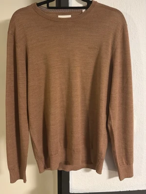 Brun stickad tröja i ullmix - Säljer en stilren brun stickad tröja med rund halsringning och långa ärmar. Tröjan har ribbade muddar vid ärmslut och nederkant. Perfekt för lager på lager och enkel att matcha med olika outfits, denna är även sprillans ny, har bara tagit bort pris lappen.