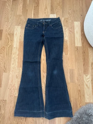 Mörkblå bootcut jeans Esprit - Snygga mörkblå bootcut jeans från Esprit med klassiska fem fickor och kontrastsömmar. Jeansen har broderad logga på insidan av linningen och är tillverkade i ett mjukt denimtyg som sitter skönt. Perfekta för dig som gillar retrovibbar och utsvängda ben.