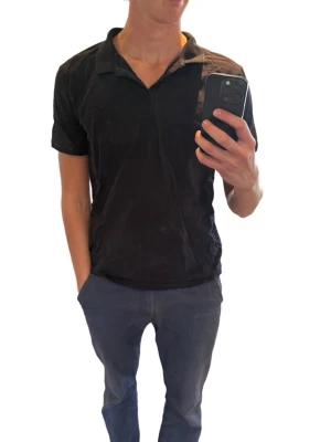 Svart kortärmad golf piké  - Klassisk svart pikétröja med krage och knappar framtill. Tillverkad i mjuk bomull och har en diskret logga broderad på bröstet. Perfekt till jeans eller shorts för en clean look.