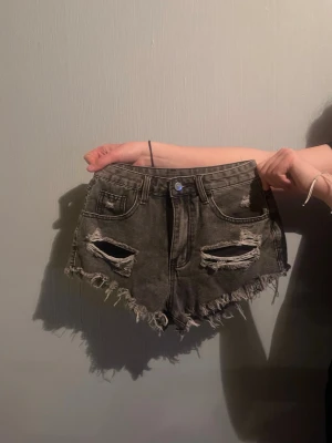 Grå slitna jeansshorts med fransar - Snygga grå jeansshorts med slitna detaljer och fransig kant. Modellen är högmidjad och har både fram- och bakfickor. 