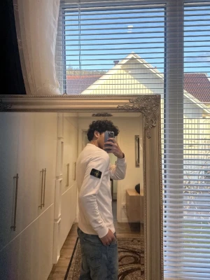 Vit tröja från Stone Island - Snygg vit sweatshirt från Stone Island med klassisk rund hals och lång ärm. Tröjan har den ikoniska svarta patchen med gult och grönt Stone Island-märke på vänster ärm. Tillverkad i mjuk bomull för en bekväm känsla.