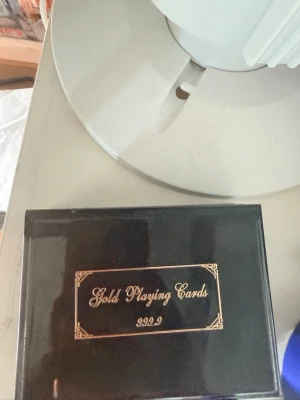 Guldspelkort i svart ask - Säljer en exklusiv kortlek med spelkort i guld-look, förpackad i en elegant svart ask med guldfärgad text 'Gold Playing Cards 999.9' på locket. Perfekt för dig som vill ha något unikt till spelkvällarna.