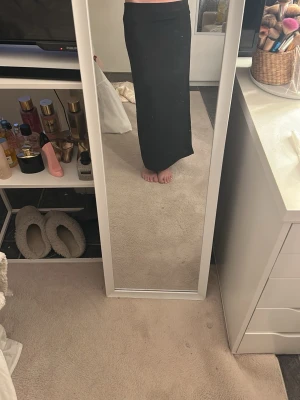 Svart långkjol med slits - Säljer en svart långkjol med slits på sidan. Kjolen har en rak och enkel design som sitter snyggt i midjan. Perfekt att styla med en crop top eller stickad tröja. Materialet känns mjukt och följsamt. Jag är 167