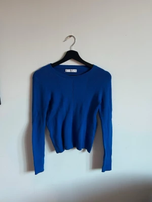 Kornblå stickad tröja med rund hals - Säljer en asnice blå stickad tröja med rund halsringning och långa ärmar från mango. Tröjan har en enkel, stilren design och är tillverkad i ett mjukt, tunt stickat material som passar perfekt till lager på lager. Perfekt för dig som gillar färg och enkelhet.