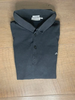 Svart J.lindeberg piké - storlek M  - Snygg svart piké från J.lindeberg i storlek m. Den  i bra skick med normalt slitage. Notera dock att den är liten i storlek så den kommer inte att passa någon med storlek M. 