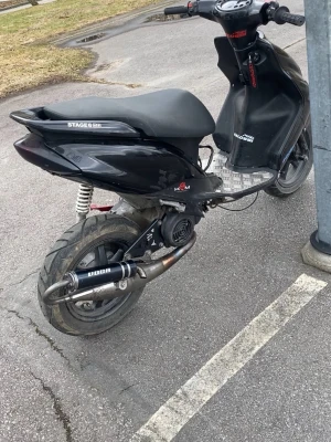 Svart Stage6 scooter med sportavgassystem - Säljer en svart Stage6 scooter med sportigt utseende och sportavgassystem från Doop. Scootern har mattsvarta kåpor, silverfärgad fotplatta och röda detaljer. Passar dig som vill ha en cool och snabb moped med stilren design.