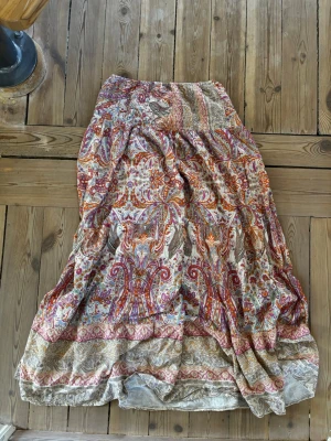 Mönstrad långkjol från Marta - Bohemisk långkjol från Marta med färgstarkt blommigt och paisley-inspirerat mönster i rött, orange, beige och lila. Kjolen har en luftig passform och är tillverkad i ett lätt, mjukt material som känns perfekt för varma dagar.