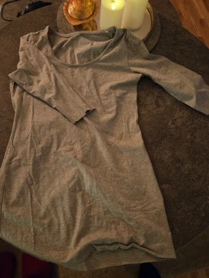 Grå trikåklänning från Esmara - En enkel och mjuk grå klänning från Esmara i trikåmaterial. Modellen har trekvartsärm och rund halsringning. Perfekt basplagg att styla med accessoarer eller jacka. Klänningen är kort och har en avslappnad passform.