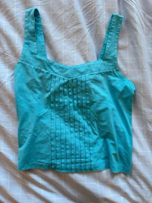Turkos ärmlös topp med veck - Snygg turkos topp med breda axelband och v-ringad hals. 