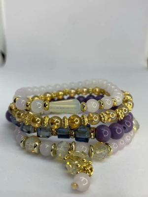 Flerfärgat pärlarmband med guldton - Snyggt armband med flera rader av pärlor i lila, vitt, blått och guldton. Armbandet har både runda och fyrkantiga pärlor samt detaljer i guld och en större kristall-liknande pärla som hänge. Ej använd utan kommer från min small business. 
