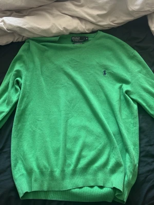Grön stickad tröja från Polo Ralph Lauren - Snygg grön stickad tröja från Polo Ralph Lauren i 100% pima bomull. Tröjan har rund halsringning, ribbade muddar och den klassiska broderade loggan på bröstet. Perfekt för dig som vill ha en stilren och bekväm look. Pris kan diskuteras.