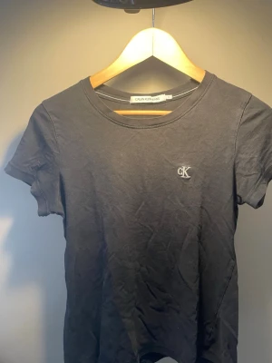 Svart Calvin Klein Jeans t-shirt - En svart t-shirt från Calvin Klein Jeans med klassisk rund hals och diskret CK-logga broderad på bröstet. Tillverkad i mjuk bomull och har en enkel, clean look som passar till allt. Perfekt basplagg för en stilren vardagsoutfit.