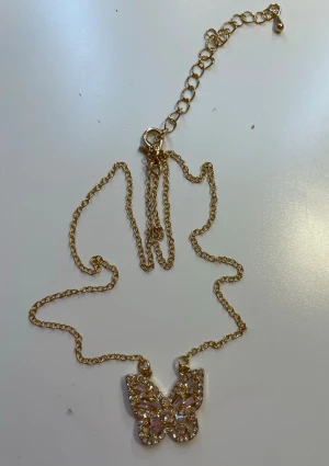 Guldfärgat glittrigt fjärilshalsband💕 - Säljer ett snyggt halsband med tunn guldfärgad kedja och ett hängsmycke i form av en fjäril. Fjärilen är dekorerad med glittrande stenar i silver 🫶🏼