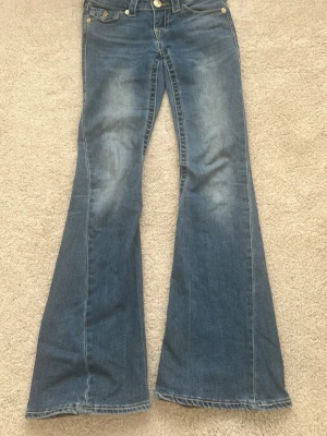 True Religion Joey Low Rise Flare Jeans - Säljer ett par blå True Religion Joey jeans med låg midja. Klassisk femficksmodell med slitningar framtill och gul kontrastsöm. Perfekta för dig som gillar Sthlm stil💖💕
