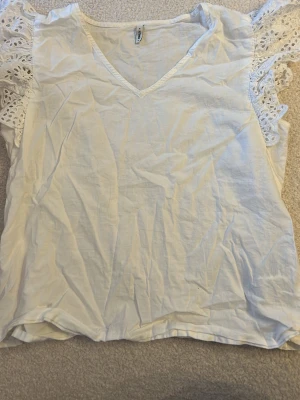 Vit blus med spetsärmar från Only - Säljer en vit blus från Only med v-ringning och korta ärmar i spets. Blusen är gjord i bomull och har en luftig passform. Perfekt för dig som gillar romantiska detaljer och en ljus look.