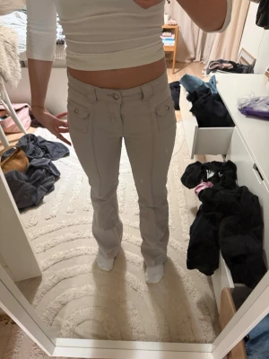 Beiga bootcut jeans med fickor - Säljer ett par snygga beiga bootcut jeans med dubbla framfickor och dekorativa knappar. Jeansen har normal midja och är i ett stretchigt material som sitter skönt. Perfekta till en enkel topp eller hoodie.