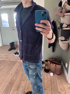 Mörkblå frottéskjorta  - Säljer en mörkblå somrig skjorta från Emmamalena i mjuk frotté. Skjortan har öppen krage, vita knappar framtill och två stora fickor. Perfekt för en avslappnad och trendig look. Materialet är bomullsfrotté som känns skönt mot huden.