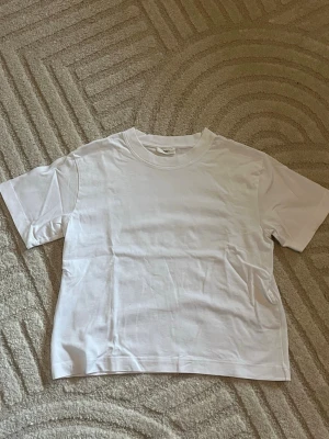Vit basic t-shirt i bomull - En klassisk vit t-shirt med rund hals och korta ärmar. Tillverkad i mjuk bomull och har en rak passform som funkar till allt. Perfekt att styla lager på lager eller bära som den är.