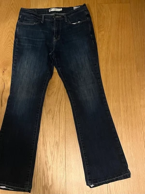 Mörkblå Bootcut jeans från Levi's med spetskanter - Mörkblå bootcut jeans från Levi's modell 532. Klassisk femficksdesign, normal midja och lätt utsvängda ben. Snygg tvätt med subtila slitningar och kontrastsömmar. Perfekta för en avslappnad men ändå stilren look.