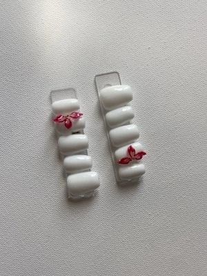 Vita press-on naglar med vinröda blad - Snygga press-on naglar i vit färg med glansig finish och dekorativa vinröda bladmotiv på två av naglarna. Naglarna har en klassisk, något rundad form och är perfekta för dig som vill ha en stilren men ändå unik look. Materialet är plast.