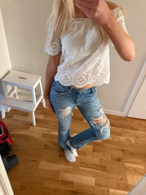 Ljusblå ripped jeans med utsvängda ben - Säljer ett par ljusblå jeans med utsvängda bootcut ben och flera slitningar och hål på framsidan. Jeansen har klassisk femficksdesign och normal midja. Perfekta för en avslappnad och trendig stil Storlek 32/34, för korta för mig som är 165cm lång. Har sytt ihop ett hål, sista bilden syns knappt. Inget jag lägger märke till❤️
