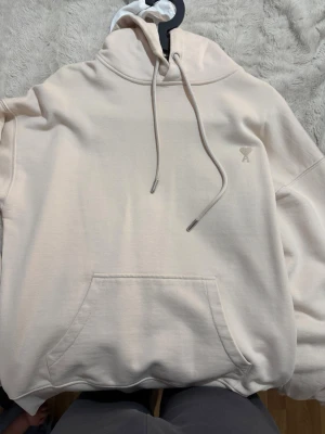 Ami hoodie - Säljer en beige hoodie från Ami med broderad logga på bröstet och 'ami' broderat i nacken. Hoodien är endast använd 2-3 gånger.