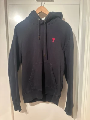 Ami Paris hoodie - Säljer en svart AMI hoodie i jättebra skick stl M. Köpt för cirka 1,5 år sedan och använd i ungefär ett år.  Hoodien är väl omhändertagen och har fortfarande mycket kvar att ge. Nypris 3000kr. Säljs nu för 700 kr, men priset är prutbart vid snabb affär.  Det finns en mindre defekt (se bild), men inget som påverkar användningen nämnvärt.  Hör av dig vid intresse eller frågor!