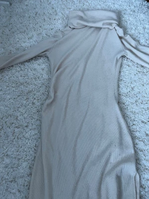 Beige ribbad långklänning Bubbleroom - Långärmad beige ribbad långklänning från Bubbleroom i storlek S. Klänningen har polokrage och är figurnära med mjukt stickat material som ger en skön känsla. Perfekt för dig som gillar stilrena och enkla plagg med en modern touch.