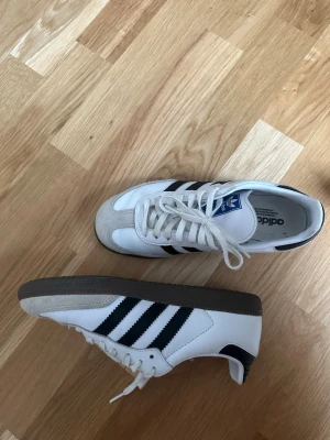 Adidas Samba  - Klassiska Adidas Samba OG sneakers i vitt läder med svarta ränder och grå mockadetaljer vid tån. Använda max 5 ggr.