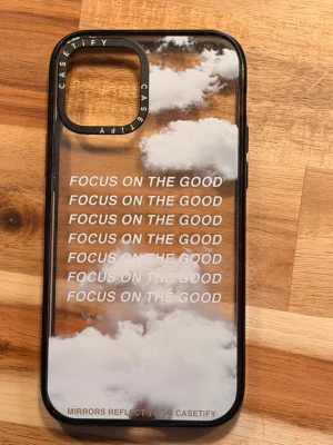 Casetify mobilskal med moln och text - Snyggt mobilskal från Casetify med transparent bakgrund, vita moln och texten 'FOCUS ON THE GOOD' upprepat i vitt. Skalets kanter är svarta och det är gjort i tålig plast. Passar perfekt för dig som vill ha ett inspirerande och stilrent skydd till mobilen.