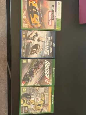 Xbox spel - Hej. Jag säljer nu ett tv-spels paket till Xbox One och 360 med två spel: MotoGP 18 och FIFA 17 Deluxe Edition. MotoGP 18 är ett racingspel med motorcyklar och officiella förare och banor från MotoGP-säsongen. FIFA 17 Deluxe Edition är ett fotbollsspel med extra digitalt innehåll jämfört med standardutgåvan. Båda spelen levereras i sina originalfodral för Xbox One. På första bilden syns även Forza Horizon för Xbox 360 och filmen Fast & Furious 5 på Blu-ray. Forza har inte kvar originalskivan.