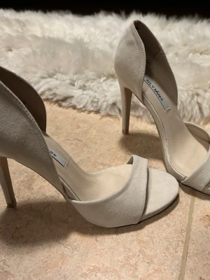 Beige klackskor, storlek 37 - Säljer ett par stilrena klackskor från NLY Shoes i beige mocka-look. Skorna har öppen tå och smal klack. Supersnygga till fest, middagar och sommarkvällar. Endast testade inomhus, nyskick, storlek 37.