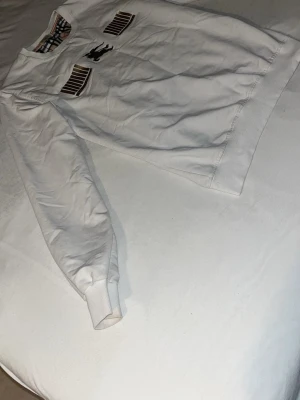 Vit sweatshirt från Burberry - Vit Burberry tröja med klassisk logga framtill och rutigt mönster vid kragen. Använd men i okej skick. Det finns några fläckar (se bilder), främst vid kragen och nedre delen. Passar bra till vardag eller som basplagg. Säljes på grund av att den inte längre används.