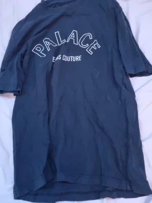 Mörkblå Palace t-shirt med tryck - Säljer en mörkblå t-shirt från Palace med vit text 'PALACE JEANS COUTURE' på bröstet och det klassiska Palace triangel-loggan i nacken. T-shirten har rund hals och korta ärmar, perfekt för en streetwear-look.