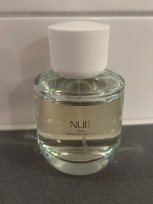 Zara Nuit Night Collection parfym - En stilren parfym från Zara Night Collection med namnet Nuit. Flaskan är rund och genomskinlig med vit kork och minimalistisk design. Innehållet är ljust och flaskan har en modern look som passar perfekt på sminkbordet.