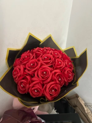Evighthets blommor - Snygg bukett med röda konstgjorda rosor, dekorerade med små pärlor i mitten av varje blomma. Buketten är inslagen i svart och gult papper och knuten med ett svart band med texten 'LOVE YOU'. Perfekt som present eller dekoration.