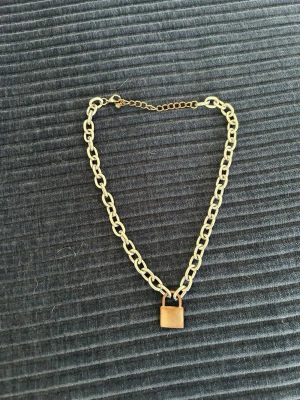 Silverfärgat kedjehalsband med låsberlock - Snyggt halsband i silverfärgad metall med grov kedja och en fyrkantig låsberlock som hänge. Justerbar längd med karbinlås. Perfekt accessoar för en trendig och edgy stil.