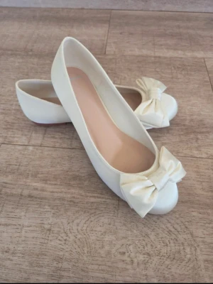 Satin ballerinaskor med rosett - Satin ballerinaskor. Polstrad innersula. Innermått är 23,4 cm. Färg ivory 