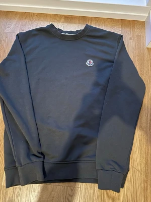 Olivgrön sweatshirt från Moncler - Klassisk olivgrön sweatshirt från Moncler med rund halsringning och diskret Moncler-logga på bröstet. perfekt för en clean och stilren look. OBS! storlek M