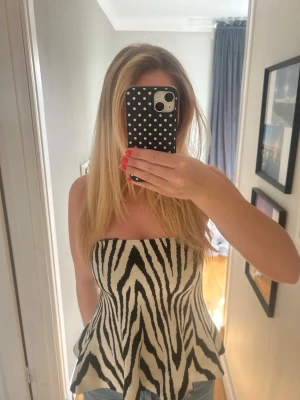 Zebramönstrad axelbandslös topp - Snygg axelbandslös topp med zebramönster i svart och vitt. Modellen är bandeau och toppen har en lätt utsvängd passform nertill. Perfekt för dig som vill sticka ut med ett djurmönster.