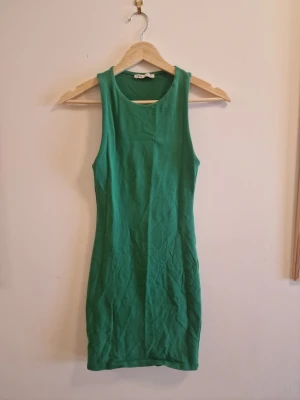 Grön ärmlös klänning från Zara - Snygg grön klänning från Zara i ärmlös modell med rund halsringning. Klänningen är kort och har en tight passform, perfekt för dig som gillar en enkel men stilren look. Tillverkad i mjuk bomull som känns skön mot huden.