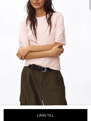 Ljusrosa topp med spetsdetaljer - Söt ljusrosa topp med korta ärmar och fina spetsdetaljer längs ärmsluten. Rund halsringning och normal passform. Perfekt för en fräsch och feminin look.