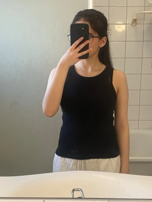 Nakd Svart ribbad linnetopp - Snygg svart ribbad linnetopp med rund halsringning och ärmlös design. Perfekt att matcha med jeans eller shorts för en enkel och stilren look. Mjuk och stretchig för skön passform.