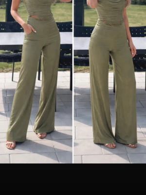 Olivgrönt sett med vida ben - Trendig olivgrönt sett med högt skuren midja och vida ben. Setter har en kroppsnära passform upptill och ärmlös design. Tillverkad i ett mjukt, stretchigt material som ger en snygg siluett. Perfekt för dig som vill ha en stilren och modern look.